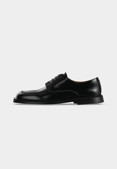 Chaussure habillée en cuir noir brillant à lacets avec une semelle épaisse et détaillée, vue de profil droit sur un fond clair uni.