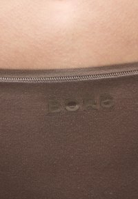 Κοντινό πλάνο ανοιχτόχρωμο δέρμα πάνω από την μέση καφέ ύφασμα με το κείμενο "BORG" τυπωμένο στο ύφασμα.