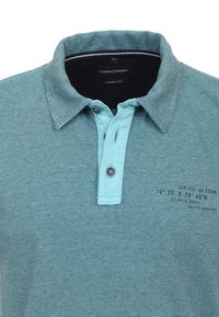 Gestreiftes Poloshirt in Türkis und Marineblau, mit Knopfleiste, kontrastierendem Kragen und bedrucktem Text auf der linken Seite. Weicher Stoff.