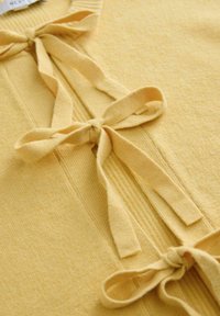 Weiches gelbes Strickgewebe mit drei gebundenen Schleifen, die vertikal entlang der Mitte verlaufen und Textur sowie Schleifendetails hervorheben.