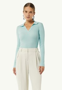 Himmelblaues, geripptes Langarmoberteil mit V-Ausschnitt und Kragen, kombiniert mit hoch taillierten cremefarbenen Hosen mit seitlichen Taschen.