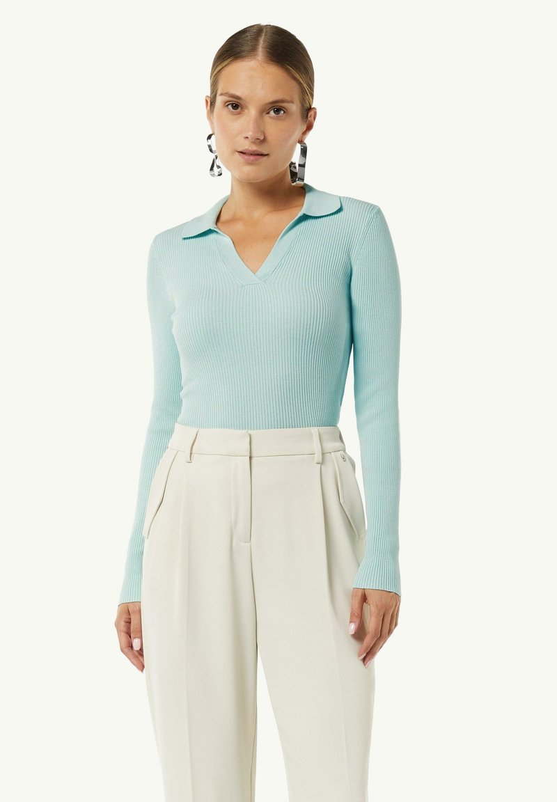 Himmelblaues, geripptes Langarmoberteil mit V-Ausschnitt und Kragen, kombiniert mit hoch taillierten cremefarbenen Hosen mit seitlichen Taschen.