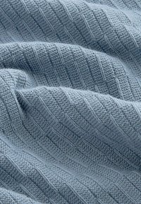 Tissu tricoté bleu clair présentant une texture à côtes verticales avec des variations subtiles d'épaisseur de fil, mettant en avant sa douceur et sa chaleur.