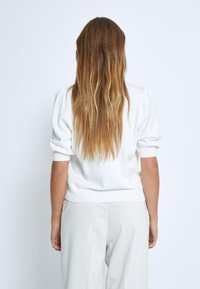 Weißer Pullover mit kurzen Puffärmeln und gerippten Bündchen, kombiniert mit hellgrauen Hosen, Rückansicht.