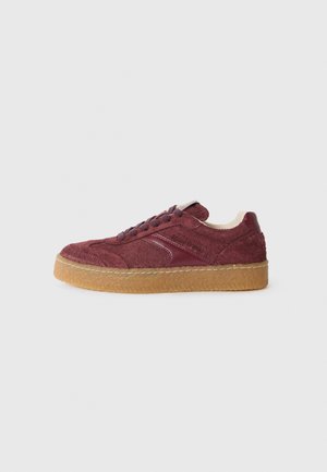 Low-top Sneaker aus burgundfarbenem Wildleder mit Gummisohle, Schnürung vorne und abgesteppten Details auf einfachem Hintergrund.