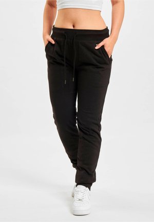 Black sweatpants made from soft material, featuring an elastic waistband, drawstring closure, and side pockets. Worn with white sneakers.