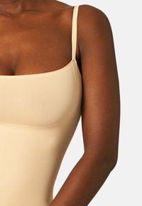Body beige senza maniche con scollatura quadrata e spalline regolabili, realizzato in tessuto morbido ed elastico con un design aderente.