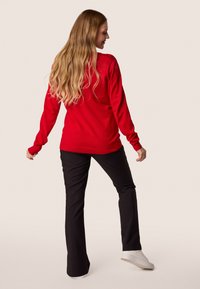 Maglione rosso con maniche lunghe e dettagli a coste, abbinato a pantaloni neri e sneakers bianche. Texture morbida, design semplice e vestibilità casual.