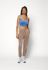 Blauwe fluwelen crop top met zilveren letters, gecombineerd met beige fluwelen joggingsbroeken. Model draagt witte sneakers en staat tegen een witte achtergrond.