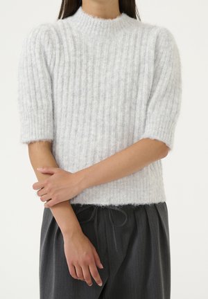 Hellgrauer, gerippter Strickpullover mit hohem Kragen und kurzen Ärmeln; weiche Textur; Saum liegt auf Taillenhöhe; kombiniert mit dunklen, weiten Hosen.