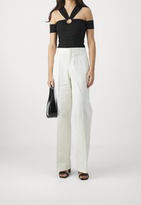 Musta olkaimeton paita, jossa on pyöreä leikkaus, yhdistettynä korkeavyötäröisiin, leveälahkeisiin valkoisiin housuihin. Asusteena musta laukku.