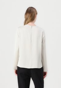 Lange mouw blouse in romige zijde met een rechte silhouet, ronde halslijn en een ritsdetail aan de achterkant. Gladde textuur met een schone afwerking.