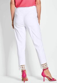 Witte enkel-lange broek met een textuur aan de onderrand, voorzien van ingewikkelde uitsnijdingen. Gepaard met roze hoge haksandalen.