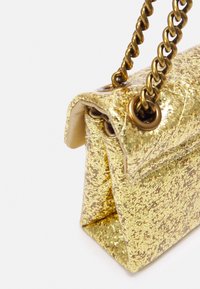 Złota torebka z brokatem z metalowym złotym paskiem przewleczonym przez okrągłe metalowe oczka na białym tle.