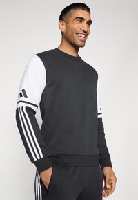 Zwart-witte sweatshirt met lange mouwen, voorzien van drie witte strepen op elke arm en een gestructureerde stof. Ribstof bij de halslijn en manchet.