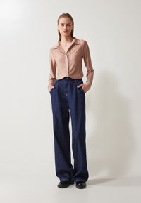 Light pink, ribbed long-sleeve shirt with a collar, paired with dark blue, wide-leg denim pants. Black shoes complete the look.