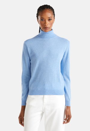 Pull col roulé bleu clair en tissu doux, doté de manches longues et d'un design ajusté. Associé à un pantalon blanc.