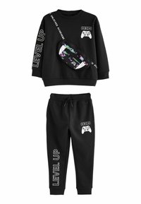 Schwarzer Trainingsanzug mit einem Langarmshirt, das weißen Text und grafische Designs aufweist, sowie passenden Hosen mit einem Kordelzug. Inklusive einer gemusterten Bauchtasche.