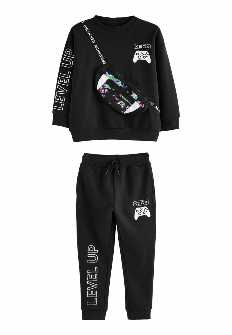 Schwarzer Trainingsanzug mit einem Langarmshirt, das weißen Text und grafische Designs aufweist, sowie passenden Hosen mit einem Kordelzug. Inklusive einer gemusterten Bauchtasche.