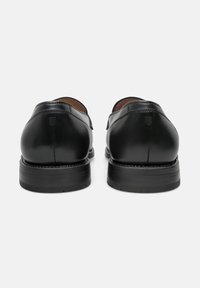 Zwarte leren schoenen met een gladde afwerking, afgeronde neus en een stevige zwarte rubberen zool, met minimale stiksels en een klein logo-detail.