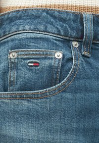 Džínsy s vybledlou modrou farbou, s malým zadným vreckom s červeno-bielo-modrým logom a medenými nitmi.