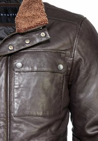 Bruine leren jas met een schapenwollen kraag, drukknopen en een borstzak, met een gladde textuur en gedetailleerde stiksels.