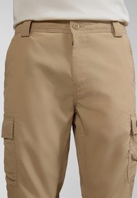 Khaki cargo bukser lavet af letvægtsstof, med knaplukning, forlommer og sidelommer med klapper. Glat tekstur.
