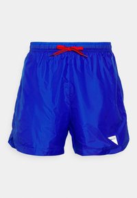 Pantaloncini da piscina blu realizzati in tessuto leggero con un motivo a quadretti, dotati di un cordoncino rosso e un'etichetta bianca con il logo sul lato.