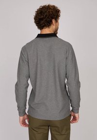 Polo gris à manches longues avec un col noir et des accents sur les épaules, présentant une texture lisse et une coupe décontractée, porté avec un pantalon vert olive.