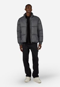 Graue Puffjacke mit hohem Kragen, Reißverschluss und gerippten Bündchen, kombiniert mit schwarzen Jeans und weißen Sneakers. Glatte Textur und Isolierung.