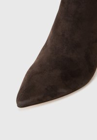 Zapato de tacón alto de ante marrón con punta afilada y textura suave, que cuenta con un tacón esbelto y un diseño sin costuras.