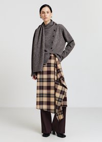 Maglione grigio lavorato a maglia con bottoni, abbinato a una gonna a quadri marrone e beige e pantaloni marroni a gamba larga. Completa l'outfit un paio di tacchi neri.