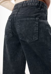 Mustat farkut, joissa on haalistunut pinta, kahdella takataskulla ja korkealla vyötäröllä. Yksinkertainen muotoilu, jossa on puhtaat linjat ja ompeleet.