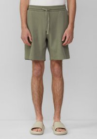 Olivgrüne Shorts mit einem strukturierten Waffelmuster, elastischem Bund und Kordelzug. Getragen mit beigen offenen Sandalen.