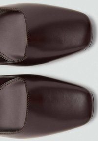 Par de zapatos de piel marrón oscuro de punta cuadrada, vistos desde arriba sobre un fondo claro.