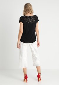 Svart topp med spetsbak, kombinerad med vita randiga culotter. Röda högklackade sandaler, slätt tyg, avslappnad passform och kort stil.