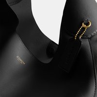 Bolso Coach de cuero negro con logo dorado y una etiqueta de cuero negro sujeta con un cierre de cadena de bolas doradas.