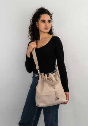 Beige leather bucket bag with a slightly darker suede base, adjustable strap, drawstring closure, and gold-tone hardware accents.