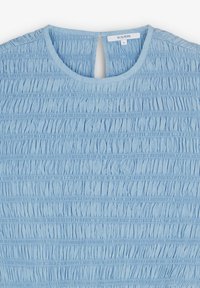 Blouse bleu clair avec texture élastique froncée, col rond, fermeture à bouton en forme de trou de clé, et petite étiquette de marque à l'intérieur du col.