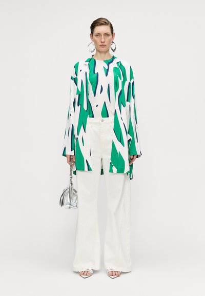 Pantalones blancos largos combinados con una camisa oversized de estampado verde y blanco. Un bolso plateado y grandes pendientes circulares completan el look.
