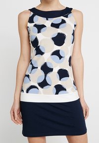 Vestido sin mangas con un estampado circular multicolor en azul claro, beige y marino, con un dobladillo inferior en marino sólido y un escote redondeado.