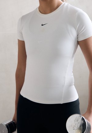 Person iført en hvid Nike-shirt og sorte bukser, der holder 3-kilos sølv håndvægte i hver hånd mod en neutral baggrund.