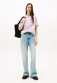 Camiseta de color púrpura claro con "TOMMY JEANS NEW YORK CITY" impreso en rosa, combinada con jeans de pierna ancha azul claro y una bolsa de tote de tejido negro.