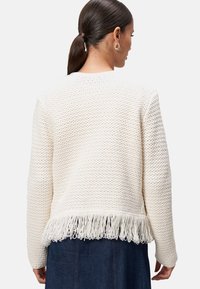 Pull en tricot blanc présentant un motif texturé et des franges le long de l'ourlet. Manches longues, col rond et coupe décontractée.