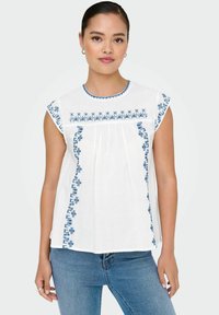 Hvid bomuldsbluse med blåt broderi langs halsudskæringen og siderne. Har korte ærmer og en afslappet pasform, med samlet stofdetalje.