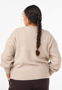 Béžový rebrovaný sveter s voľným strihom, širokými rukávmi a pevnou pletenou textúrou, zobrazený zozadu. Má okrúhly výstrih a viditeľné švové detaily.