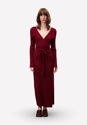 Gebreide, diep rode wikkeljurk met lange mouwen en een tailleceintuur, voorzien van een V-hals en een designs tot op de vloer. Voorzien van een gestructureerde afwerking.