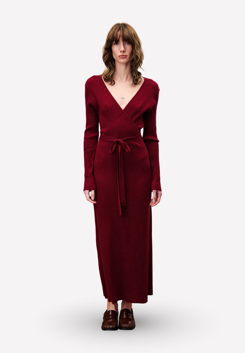 Gebreide, diep rode wikkeljurk met lange mouwen en een tailleceintuur, voorzien van een V-hals en een designs tot op de vloer. Voorzien van een gestructureerde afwerking.