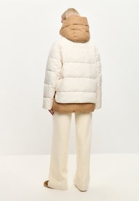 Puffjakke i crème med hætte i brun, med quiltet design og afslappet pasform. Sammen med crème brede bukser og brune slides.