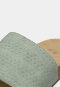 Πράσινο δερμάτινο σανδάλι slide με υφή ανάγλυφης, ανώμαλης επιφάνειας και καφέ, μαλακό πέλμα. Ο σχεδιασμός περιλαμβάνει ελάχιστες ραφές κατά μήκος των άκρων.